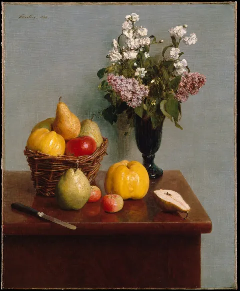 A tabletop still life of a fruit basket beside a vase of white and pink lilac blossoms.